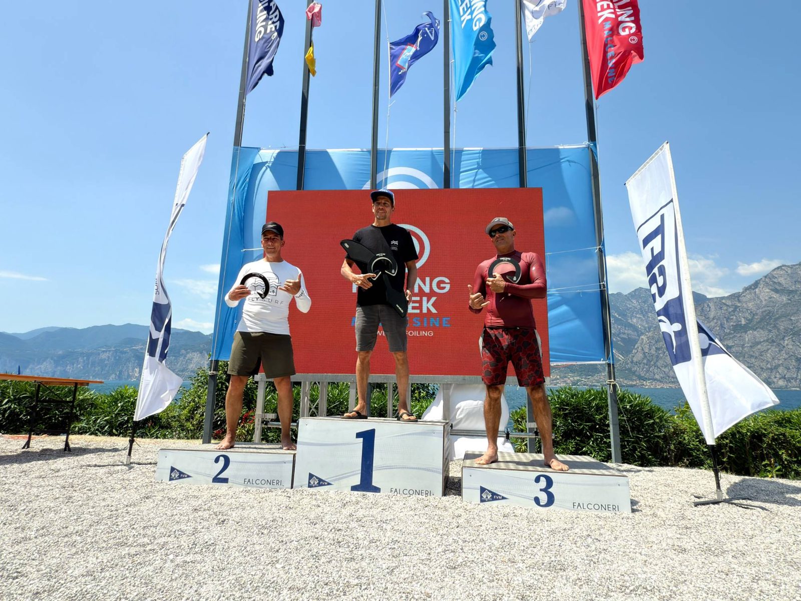 Drie rijders op het podium voor een rood scherm met vlaggen en bergen op de achtergrond; Piet Varkevisser staat links op plek 2